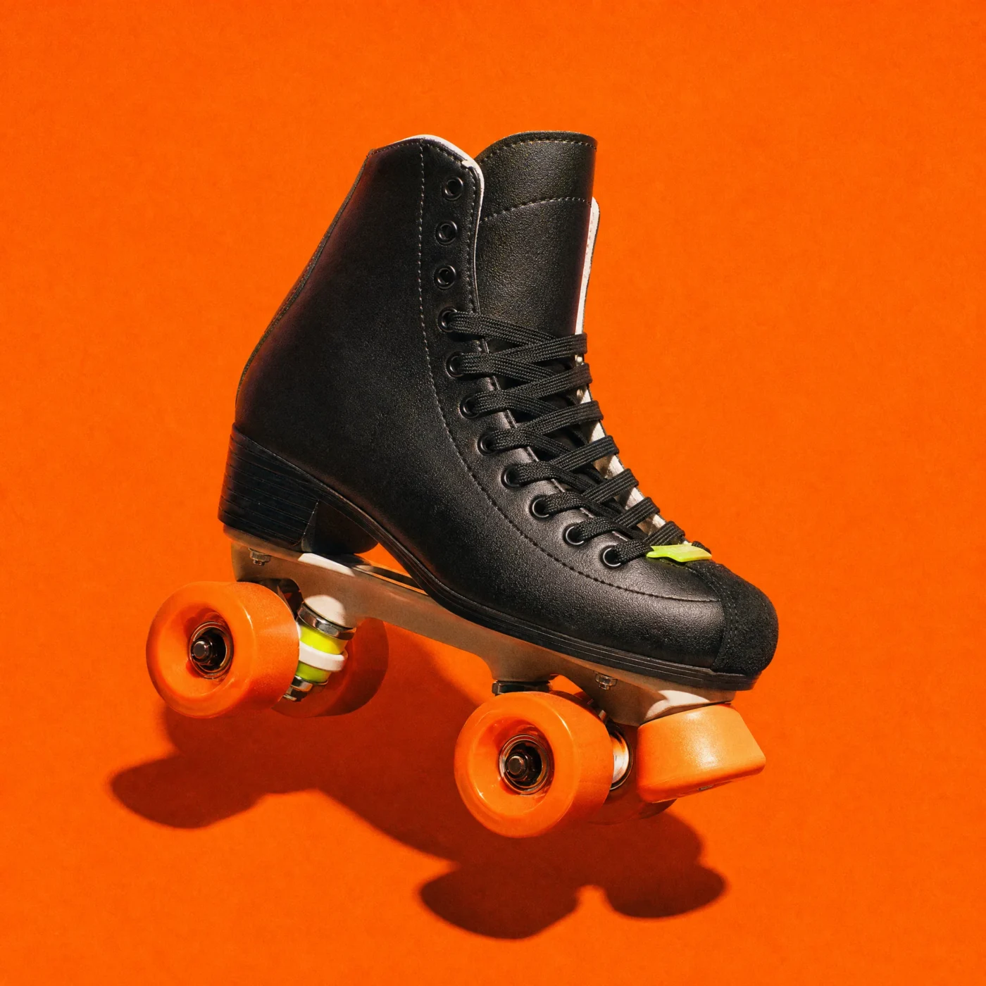 A single black quad skate with orange wheels on a flat orange background