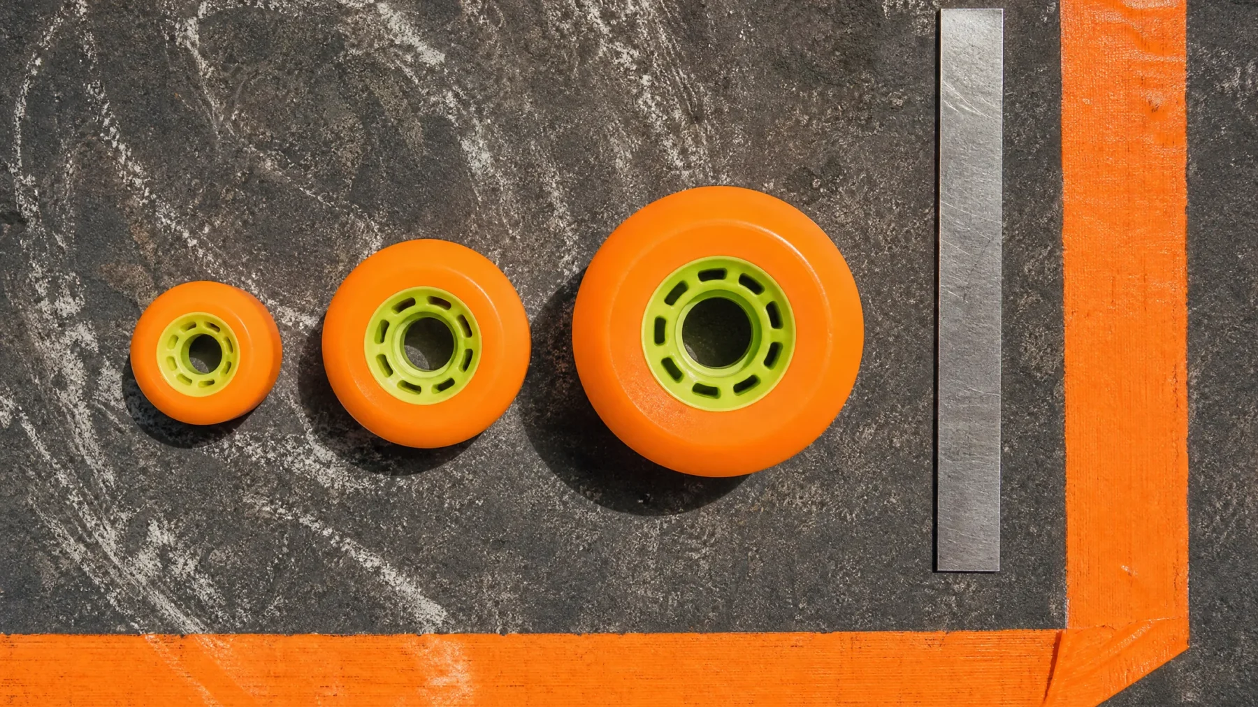 Three sizes of quad skate wheels lined up beside a plain ruler